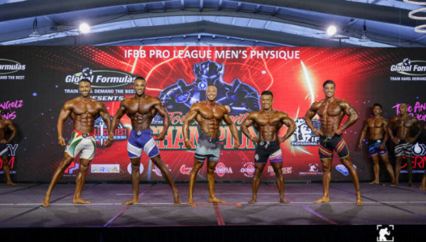 Six male bodybuilders posing on a stage in front of a large red and black IFBB Pro League Men's Physique championship backdrop.